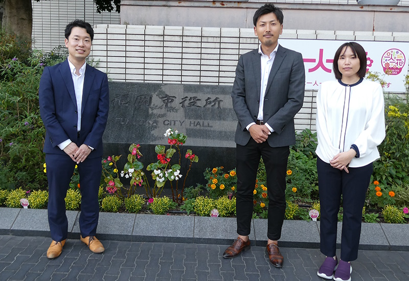 福岡市役所前に立つ浜田さん（左）、篠崎さん（中央）、栗本さん（右）